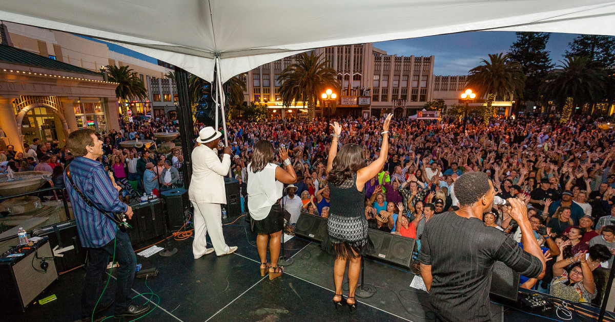 Live band performs at Courthouse Square in Redwood City during a summer concert with a packed crowd cheering.