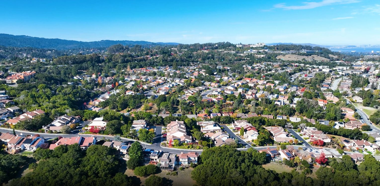 Aerial view of Sugarloaf San Mateo neighborhood showing hillside homes, mature trees, and Bay Area mountain backdrop with contemporary ranch-style houses on generous lots